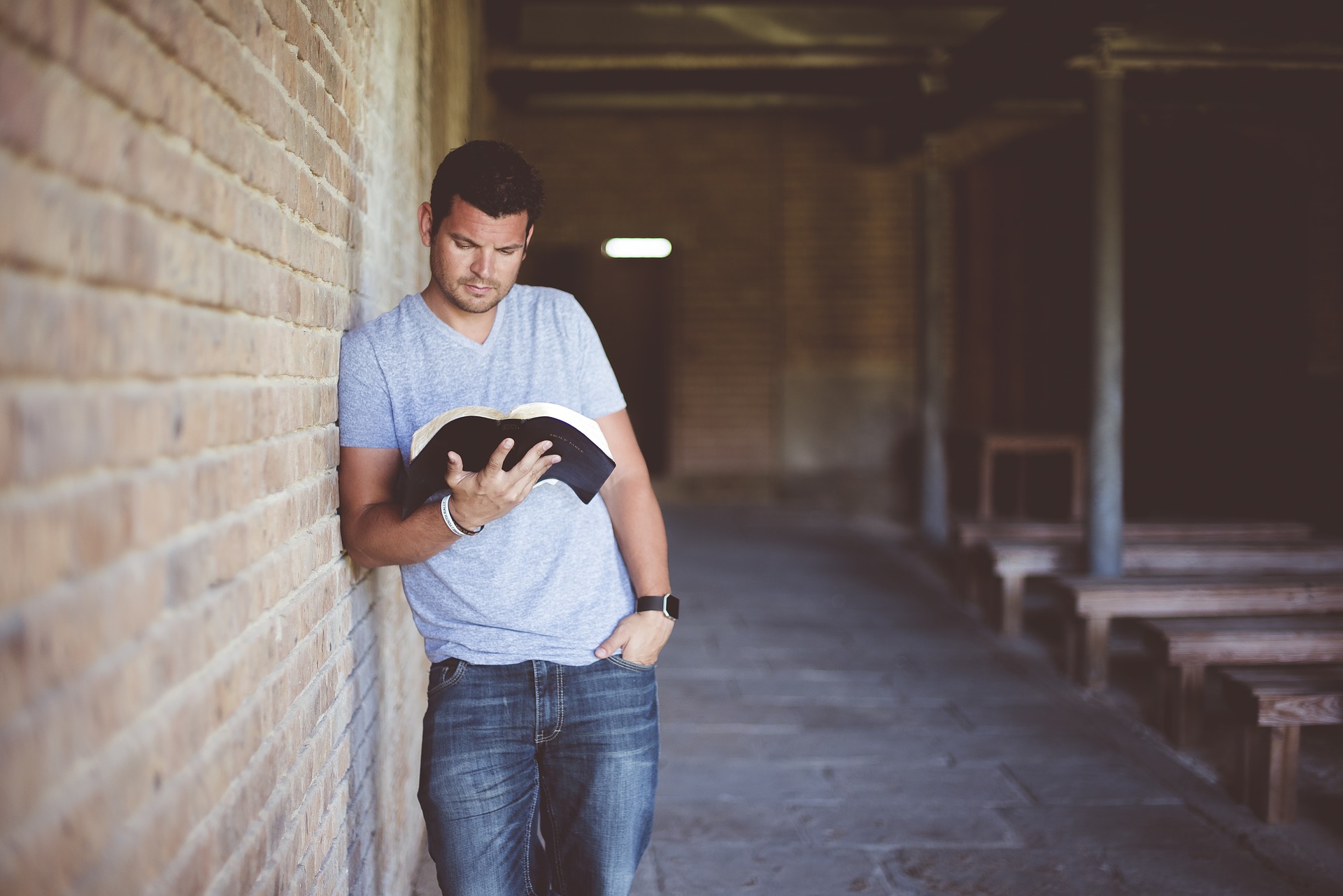Mann lehnt an einer Mauer und liest in einem Buch