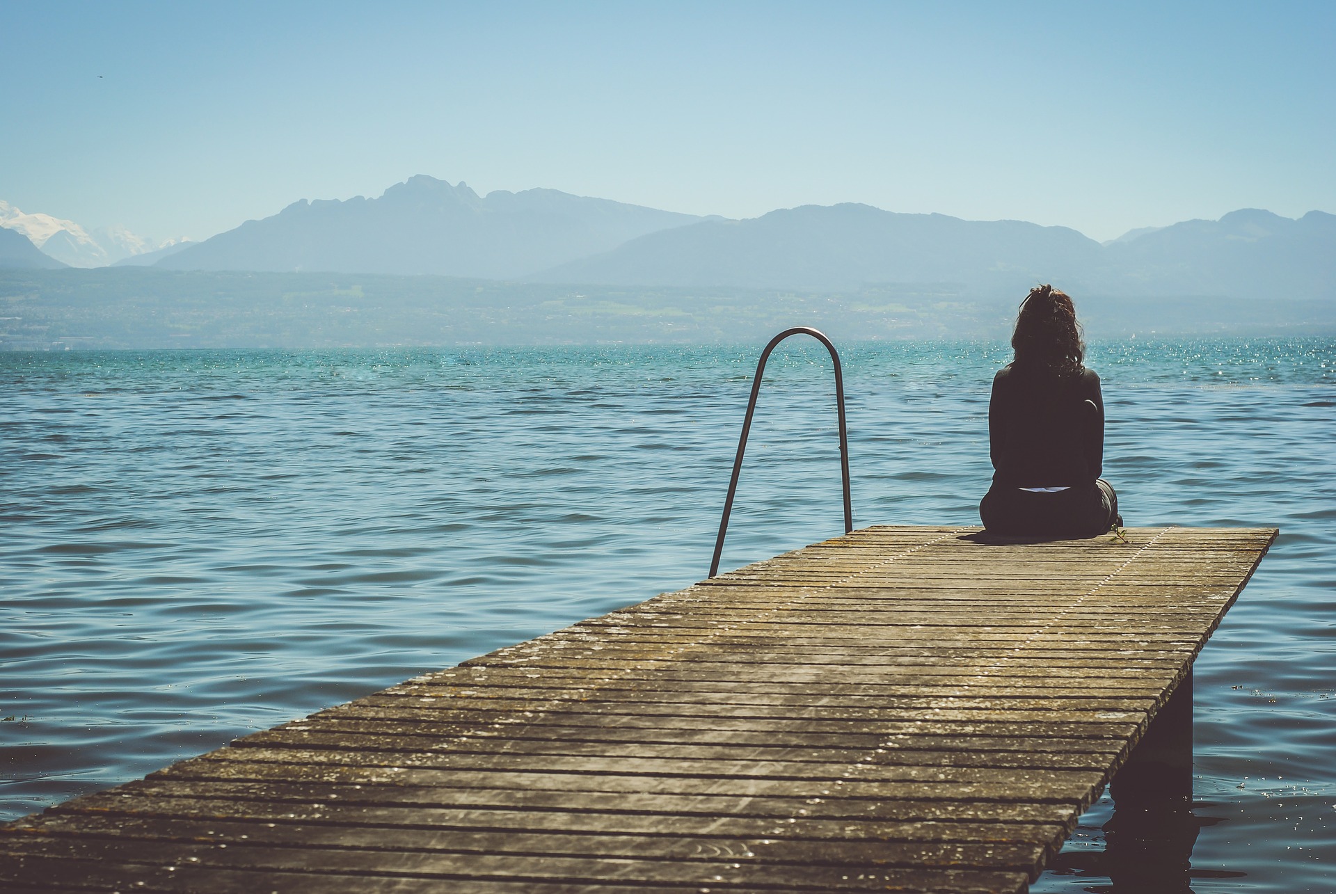 alone-1868559_1920 Frau sitzt auf einem Steg am Wasser, schaut ruhig in die Berge als Sinnbild dafür, wie man seine Depression überwinden kann