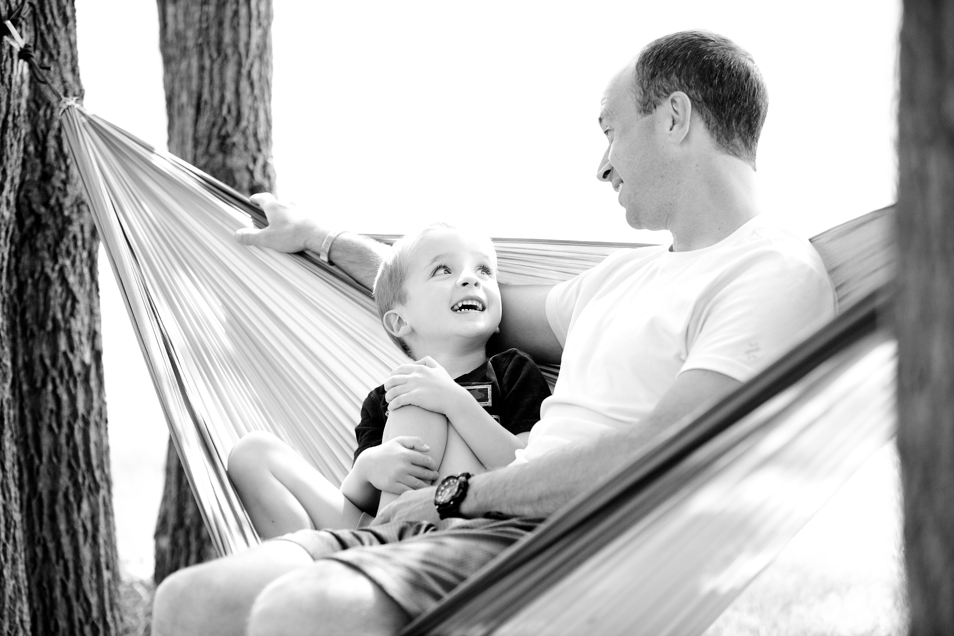 father-1633655_1920 Vater und Sohn sitzen zusammen in der Hängematte und lächeln sich liebevoll an