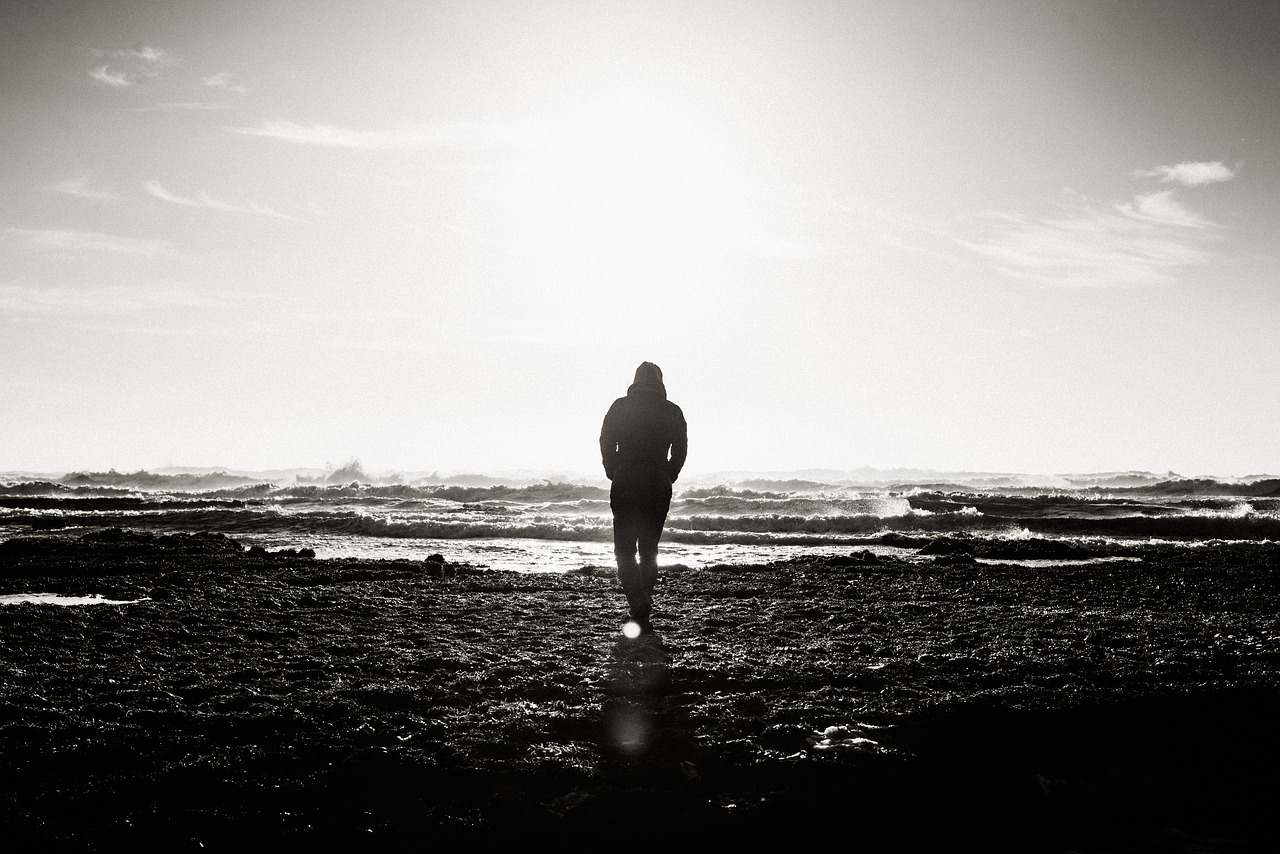 Mann am Strand in schwarz-weiß, die Wellen vor ihm als Sinnbild für Gedanken, mit denen wir uns selbst blockieren