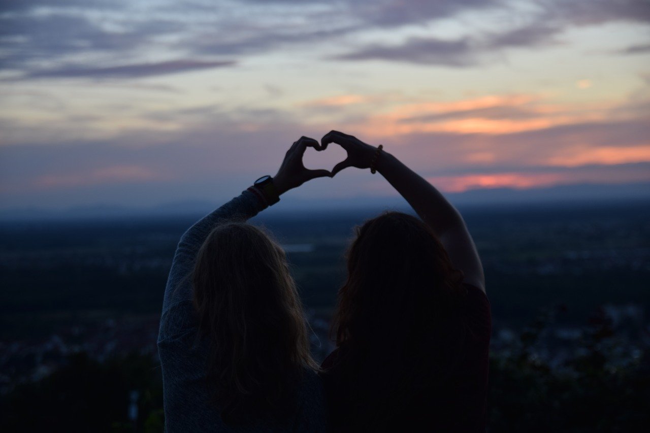 Zwei Mädchen halten ihre Hände als Herz gemeinsam in den dunklen Abendhimmel