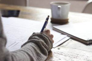 Arm mit Kuli in der Hand, schreibt, eine Tasse im Hintergrund