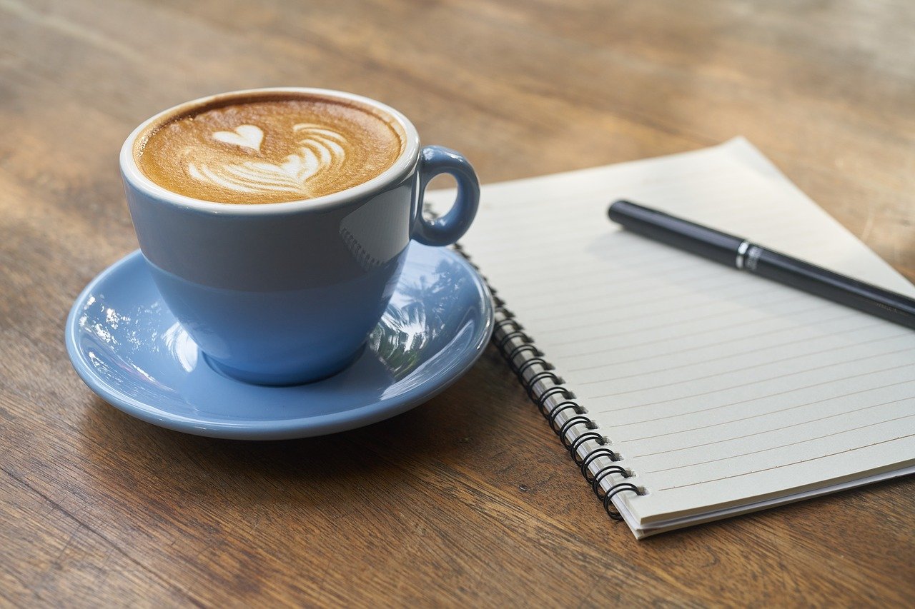 Tasse Kaffee und Heft mit Stift als Sinnbild für Schreiben als Selbstcoaching