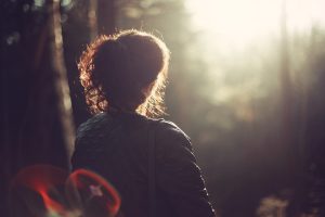 Frau im Wald von hinten sichtbar im sanften Licht 