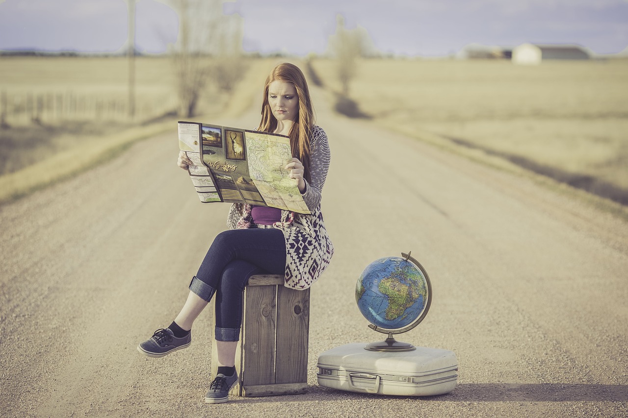 2024-8 globe-trotter-1828079_1280 Frau auf der Straße sitzt auf einem Koffer mit Landkarte in der Hand und Globus neben sich als Sinnbild für ihre Heldenreise